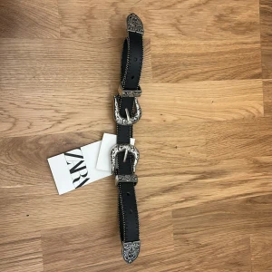 Svart skärp med silverdetaljer från Zara - Säljer ett snyggt svart skärp från Zara i 100% läder. Det har coola silverdetaljer på spännena och ändarna, vilket ger en unik look. Perfekt för att piffa upp vilken outfit som helst! 🖤