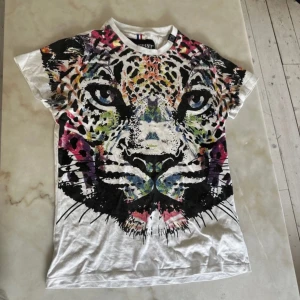 Vit t-shirt med leopardtryck från Horspist - Säljer en cool vit t-shirt från Horspist med ett stort, färgglatt leopardtryck på framsidan. T-shirten har korta ärmar och är perfekt för en avslappnad stil. Den är i bra skick och passar perfekt för sommardagar eller en utekväll.