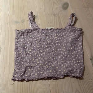 Lila prickig topp från Kappahl - Säljer en söt lila topp från Kappahl med små vita prickar. Toppen är i ett stretchigt material med smockdetaljer och har smala axelband. Perfekt för sommardagar eller som ett lager under en kofta. Använd få gånger och i mycket bra skick!