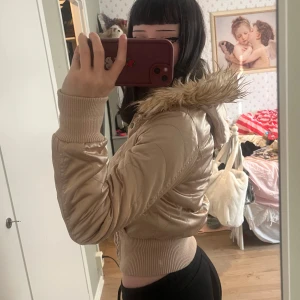 Beige pufferjacka med fuskpäls, y2k, mcbling - Säljer en snygg beige pufferjacka med fuskpäls på huvan. Jackan är croppad och har en tight passform med ribbade muddar. Perfekt för höst och vinter! Den har knappar och dragkedja framtill för extra värme. Superfin och i mycket bra skick!