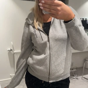 Grå zip från Sail racing - Säljer en snygg grå zip från sail racing i mycket bra skick. Den har en dragkedja framtill och långa ärmar. Passar till både chill och lite mer uppklädda tillfällen. Det är en litet defekt som inte märks alls men fickan sitter ej fast inifrån men de gör ingen skillnad, storlek 176 sitter som s/m🩶