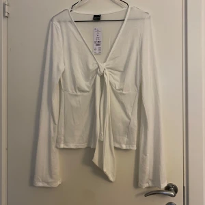 Vit långärmad topp från Gina Tricot - Säljer en stilren vit långärmad topp från Gina Tricot i storlek M. Toppen har en snygg knytning framtill och är perfekt för både vardag och fest. Materialet är mjukt och bekvämt. Ny med taggar kvar! Säljer även en brun 