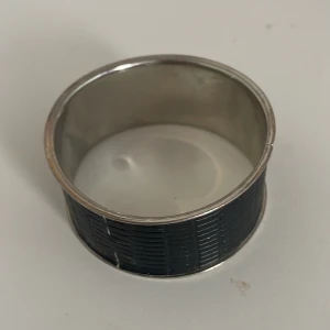 Bred svart armband i metall - Snyggt och stilrent brett armband i metall med en svart yta som har ett diskret mönster. Perfekt för att ge en elegant touch till vilken outfit som helst. Armbandet är i bra skick och passar både till vardags och fest.