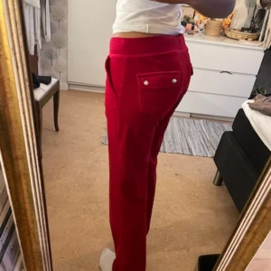Röda Juicy mjukisbyxor med snörning - Säljer ett par snygga röda Juicy mjukisbyxor i mycket bra skick. De har en bekväm loose passform och är perfekta för mysiga dagar. Byxorna har snörning i midjan och en liten broderad detalj på fickan. Supermjuka och sköna!