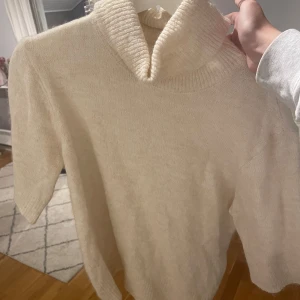Beige stickad polotröja från Soyaconcept - Mysig beige stickad polotröja från Soyaconcept. Perfekt för kyliga dagar med sin mjuka och varma känsla. Tröjan har en klassisk polokrage och korta ärmar, vilket gör den både stilren och bekväm. Passar perfekt till både vardag och lite finare tillfällen.