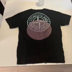 Säljer en svart t-shirt från Stone Island med deras ikoniska logga i stort tryck på baksidan och ett litet tryck på framsidan. Perfekt för en casual look. T-shirten är i bra skick och passar till både vardag och fest. Pris går att diskutera.