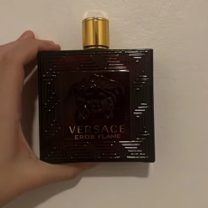 Versace Eros Flame Parfym - Säljer en elegant Versace Eros Flame parfym i en fyrkantig, röd flaska med guldlock. Flaskan har ett snyggt mönster och den ikoniska Versace loggan Perfekt för den som vill ha en doft som sticker ut. Har använt cirka 60 ml så har kvar runt 140 ml av den 200 ml flaskan.