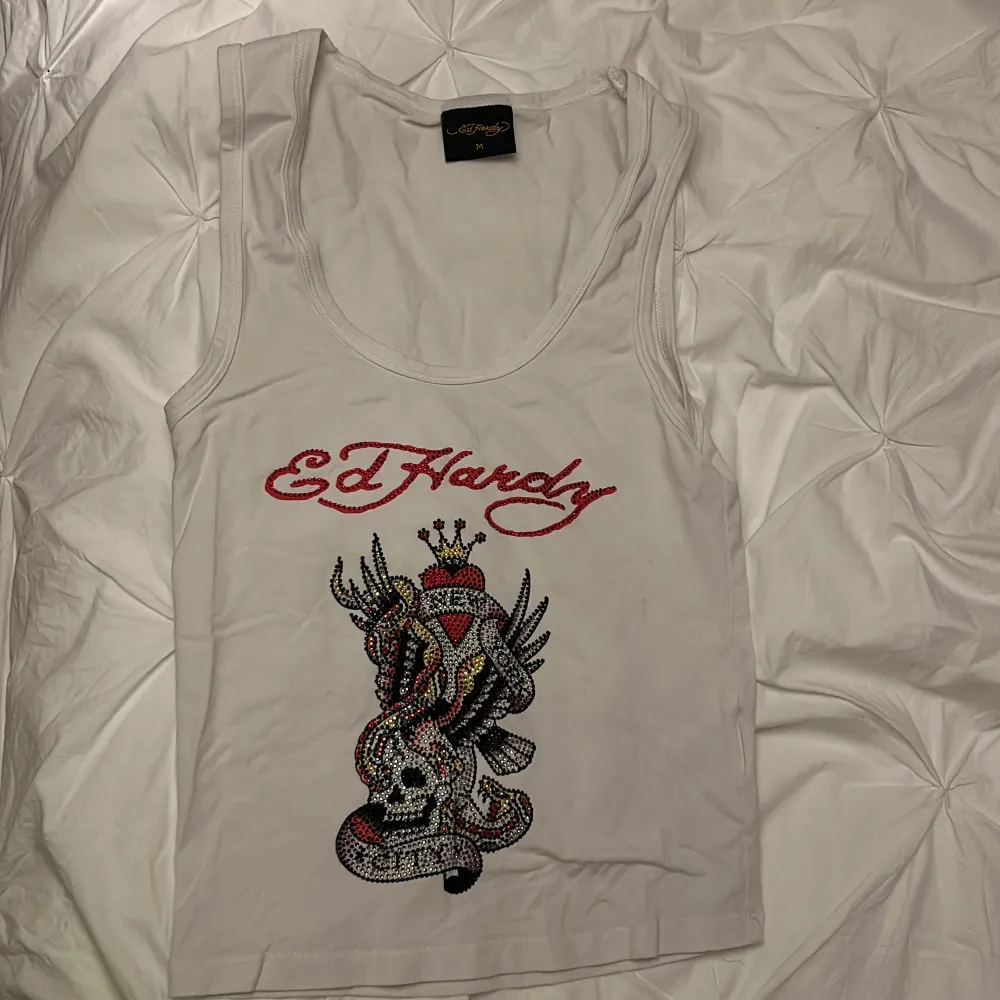 Säljer en cool vit linnetopp från Ed Hardy med ett stort, färgglatt tryck av en dödskalle! Köpte för ca 700kr och det är näst intill oanvänt. Ser ut som vintage ed Hardy! Går inte ner i pris!. Toppar.