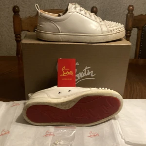 Vita sneakers med nitar från Christian Louboutin - Säljer ett par vita sneakers från Christian Louboutin ganska bra skick får med 7 extra spikar i påse. Storlek 40-41.     