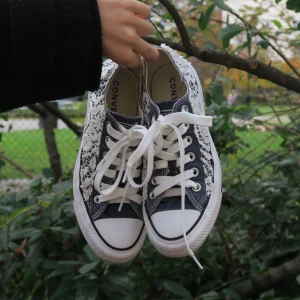 Converse sneakers med spetsdetaljer - Säljer ett par unika Converse sneakers i marinblå och vitt med snygga spetsdetaljer. De har klassisk snörning och en bekväm passform. Ger en cool touch till vilken outfit som helst!