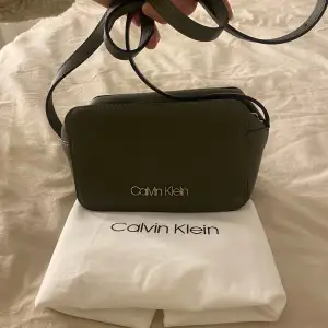 Snygg grön axelväska från Calvin Klein i mycket bra skick. Väskan har en stilren design med dragkedja och justerbar axelrem. Perfekt för både vardag och fest! Kommer med originalpåse.