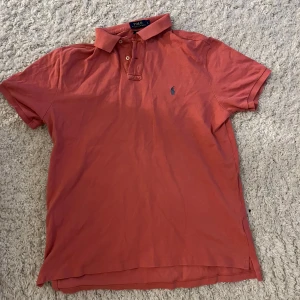 Röd pikétröja från Ralph Lauren - Säljer en snygg röd pikétröja från Ralph Lauren i storlek L. Tröjan har en klassisk krage med knappar och det ikoniska broderade logotypen på bröstet. Perfekt för både vardag och fest! 🐎