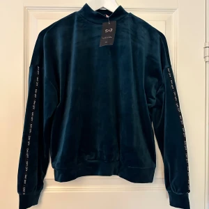 Mörkgrönt jul velourset från Hunkemöller  - Säljer ett supermjukt och skönt mörkgrönt jul velourset från Hunkemöller. Tröjan har långa ärmar med text längs sidorna och en hög krage. Perfekt för en avslappnad dag eller mysiga stunder hemma. Setet är i nyskick och har prislapparna kvar. Passar perfekt till höst och vinter, speciellt julen🎄