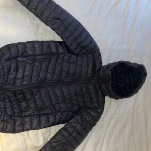 Marinblå peak performance dunjacka med huva - Säljer en marinblå dunjacka i mycket bra skick. Den har en praktisk huva och dragkedja framtill. Perfekt för kyliga höst- och vinterdagar. Jackan är lätt och bekväm att bära.