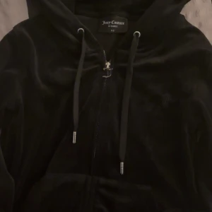 Svart velour zip hoodie från Juicy Couture - Säljer en supermjuk och snygg svart velour zip jacka från Juicy Couture i storlek XS. Den har dragkedja och huva med snören. Perfekt för en avslappnad och stilren look. Passar både till vardags och festliga tillfällen. 🖤I jätte bra skick, inga hål och inte så så mycket använd. Nypris: 1300kr säljer för 730kr men pris kan diskuteras.