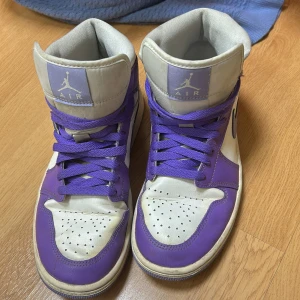 Lila och vita Nike air jordans - Säljer ett par coola Nike Air sneakers i lila och vitt. De har en hög modell med snörning och den klassiska Nike-loggan på sidan. Skorna är i bra skick med lite slitage på sulan. Perfekta för både vardag och fest!