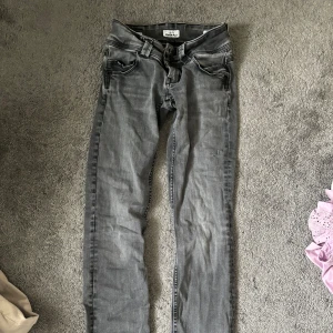 Svart gråa jeans från Pepe Jeans - Säljer ett par svarta gråa jeans från Pepe Jeans i bra skick. De har en snygg, sliten look med detaljerade bakfickor och en liten reva på benet, som har till mesta dels lagats. Lågmidjade jeans, som passar till både vardag och fest! Kontakta för mer💗