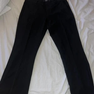 Svarta kostymbyxor från BikBok - Snygga svarta lågmidjade kostymbyxor (Vera) från BikBok i storlek 40. Perfekta för både jobb och fest! De har en klassisk design med en rak passform och är tillverkade i ett bekvämt material. Passar utmärkt till höst- och vintergarderoben. Dessa är helt nya och oanvända, säljer pågrund av att dessa är för korta