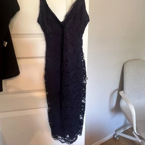 Mörkblå spetsklänning - Säljer en elegant mörkblå spetsklänning med smala axelband och v-ringning. Klänningen har en figurnära passform och är perfekt för festliga tillfällen. Den är i mycket bra skick och har en vacker spetsdetalj.