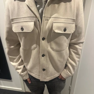 Beige overshirt med knappar - Säljer en snygg beige overshirt i mycket bra skick. Den har en stilren design med knappar framtill och två stora bröstfickor. Perfekt för höst och vår, och funkar både till vardags och lite finare tillfällen. Passformen är normal och materialet känns mjukt och bekvämt. Från zara. Storlek L. Köpt fel storlek så endast testad