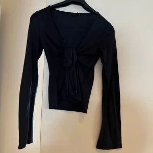 Mörkblå  långärmad topp med knyt från Gina - Snygg mörkblå långärmad topp med knyt framtill. Perfekt för både vardag och fest. Den har en tight passform som framhäver figuren och är gjord i ett mjukt och bekvämt material.