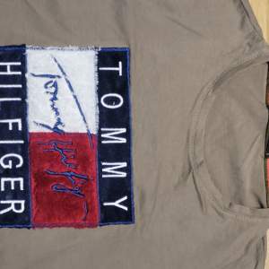 Säljer en snygg grå t-shirt från Tommy Hilfiger med ett stort, färgglatt logotryck på bröstet i blått, vitt och rött. T-shirten är kortärmad och perfekt för en avslappnad stil. Passar bra till både jeans och shorts!