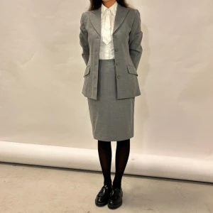 Grå kavaj och kjol från Miss Philippe - Säljer en elegant grå kavaj och matchande kjol från Miss Philippe. Kavajen har tre knappar och klassiska slag, medan kjolen är knälång med en diskret slits bak. Perfekt för kontoret eller formella tillfällen. Både kavajen och kjolen är i mycket bra skick och ger en stilren look.