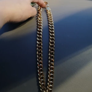 Guldduble halsband 55 cm - Halsband med breda länkar. Perfekt för att ge en extra touch till din outfit, oavsett om det är till vardags eller fest. Halsbandet har en robust känsla och en glansig finish som verkligen fångar ljuset. Passar både till casual och mer uppklädda tillfällen.
