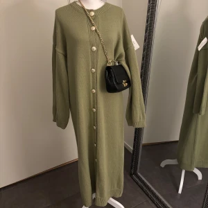 Knitwear Golden Button Dress | Olive Green - Hej! Detta är mitt företag, och du kan köpa produkten här på plick eller via vår hemsida: Nooralanna.com. Det pris som anges är fast, och jag kommer inte att svara på meddelanden om budgivning. Tack för förståelsen! 	•	Färg: Grön 	•	Längd: 133 cm        •     Kan öppnad och användas som cardigan 	•	Lagerstatus: 2 st kvar  Retur gäller endast via beställning på hemsidan. Läs retur policy vad som gäller.   Kontakta mig gärna vid seriösa frågor eller köp. Tack!
