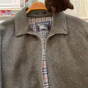 Grå ulljacka från Burberry - Säljer en snygg grå ulljacka från Burberry i mycket bra skick. Jackan har en klassisk krage och stängs med dragkedja. Insidan har ett stilrent rutigt mönster. Perfekt för höst och vår! Köpte denna bagagnad från hemsidan vestiare. Har knappt använt då den är lite passar perfekt i armarna men lite kort i längden, jag är 187. Storlek L/M. Skick 9/10.