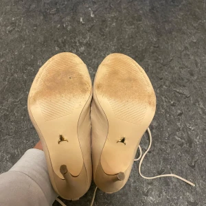 Beige klackskor med snörning - Snygga beige klackskor i skinn med coola utskärningar och snörning. Perfekta för festliga tillfällen! De har en spetsig tå och hög klack som ger en elegant look. Skorna är i bra skick med lite slitage på sulorna.