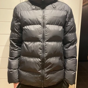 Svart vinterjacka från J.Lindeberg - Säljer en snygg svart pufferjacka från J.Lindeberg i mycket bra skick. Jackan har en dragkedja framtill och är perfekt för kalla vinterdagar. Den är varm och har en skön huva för extra värme. Perfekt för dig som vill hålla stilen i vinter! Pufferjacka alltså ej dun