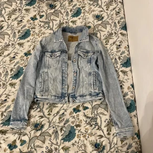 Ljusblå jeansjacka från FB Sister - Säljer en snygg ljusblå jeansjacka från FB Sister i storlek S. Jackan har en klassisk design med knappar framtill och två bröstfickor med lock. Perfekt för vår och sommar, och ger en cool touch till vilken outfit som helst. Använd men i bra skick!