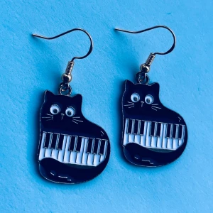 Svarta kattörhängen med pianotangenter - Supercoola örhängen i form av svarta katter med pianotangenter. Nickelfria krokar. Hämtas i Hornstull i Stockholm eller skickas mot fraktkostnad. 🐈‍⬛