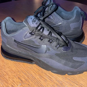 Svarta Nike sneakers - Säljer ett par svarta Nike sneakers i mycket bra skick. De har en snygg och modern design med en stor luftdämpning i sulan för extra komfort. Perfekta för både vardag och träning. Skorna har snörning och är gjorda i syntetmaterial.