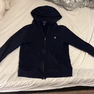 Mörkblå hoodie från Ralph Lauren storlek xs/ 14-16 år  - Säljer en snygg mörkblå hoodie från Ralph Lauren i storlek L. Den har en dragkedja framtill och en klassisk huva. Perfekt för kyliga dagar och har en liten logga på bröstet. Superbekväm och stilren! 💙