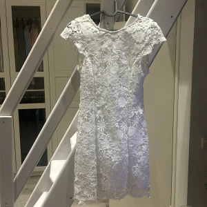 Vit spetsklänning med öppen rygg - Säljer en superfin vit spetsklänning med korta ärmar och en elegant öppen rygg. Perfekt för sommarens fester eller studentfiranden. Klänningen har ett vackert blommigt mönster och är i mycket bra skick. Passar perfekt för en chic och romantisk look!