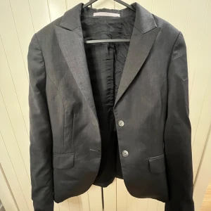 Svart kavaj från Tiger of Sweden - Snygg svart kavaj från Tiger of Sweden i mycket bra skick. Perfekt för både formella och semi-formella tillfällen. Kavajen har en klassisk design med två knappar framtill och fickor. Passar utmärkt till höst- och vintergarderoben. Hör av dig vid fler frågor🩷