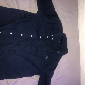 Mörkblå skjorta från GANT - Säljer en snygg mörkblå skjorta från GANT i bra skick. Skjortan har vita knappar och ett broderat GANT-märke på bröstet. Perfekt för både vardag och fest! Passar ungdomar i åldern 13-14 år.