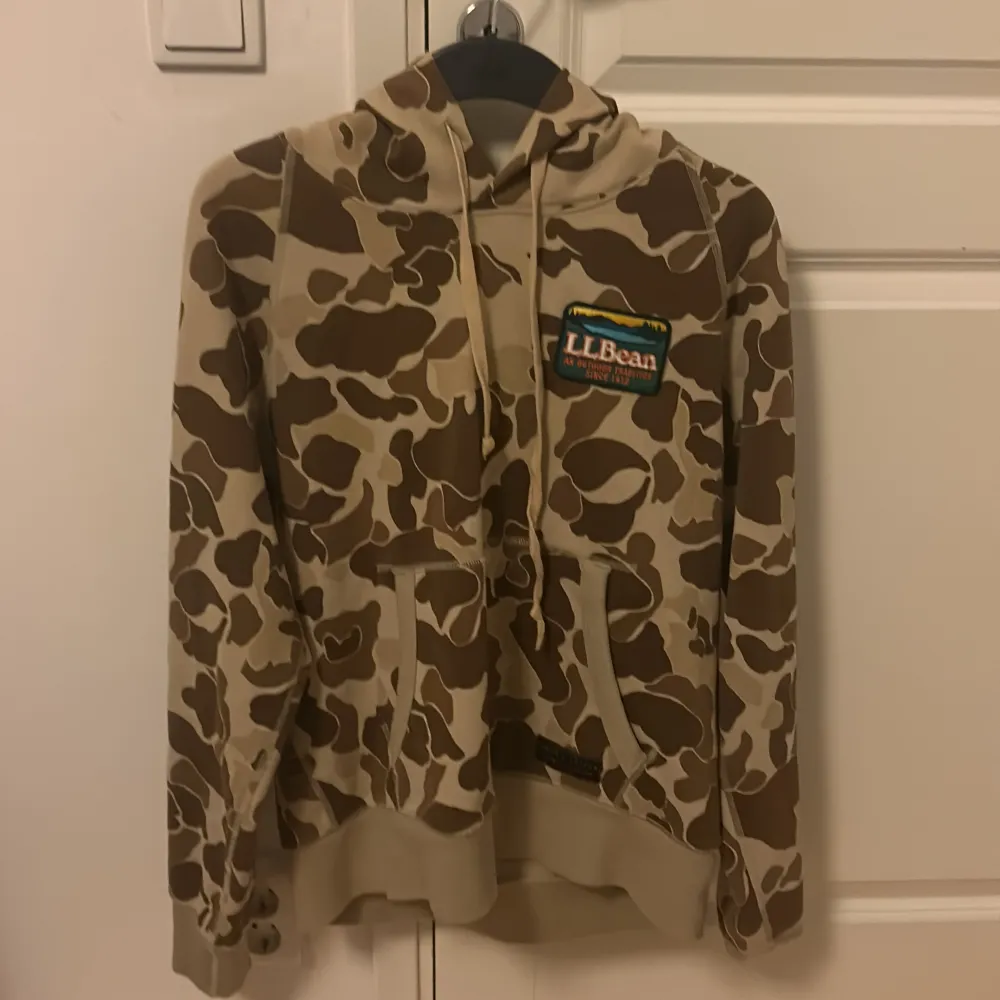 Säljer en snygg och unik camouflage hoodie från L.L. Bean i samarbete med Todd Snyder. Den har en klassisk känguruficka och justerbar huva. Perfekt för en avslappnad stil eller utomhusäventyr. Passar bra till både höst och vår!. Tröjor & Koftor.