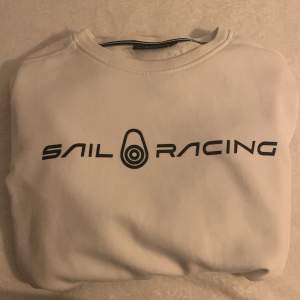 Säljer en snygg vit tröja från Sail Racing. Den har en stilren design med loggan tryckt i svart på framsidan och en liten detalj på baksidan. Perfekt för en casual look eller när du vill ha något bekvämt men ändå stiligt. Tröjan är långärmad och gjord i ett mjukt material.