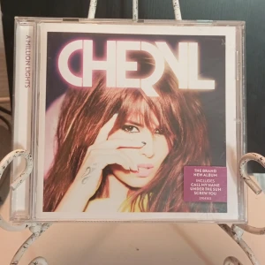 A Million Lights av Cheryl - CD-albumet 'A Million Lights' av Cheryl innehåller låtar som 'Under the Sun', 'Call My Name', och 'Screw You'. Albumet har en färgglad design med en bild av Cheryl på framsidan.