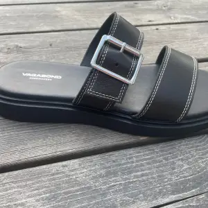 Säljer ett par snygga svarta sandaler från Vagabond. De har en stilren design med två breda remmar och en justerbar spänne i silver. Perfekta för sommaren och passar till både vardag och fest. Sandalerna är i helt nya och kommer i originalförpackning. Orginal pris är 899 men säljer för 600. Men pris kan diskuteras.