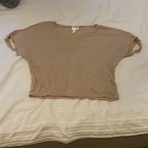 Beige linnetopp från H&M - Säljer en superfin beige linnetopp från H&M. Den är kortärmad och har en v-ringad design. Toppen är croppad och har en snygg knytning framtill som ger en avslappnad look. Perfekt för sommardagar!