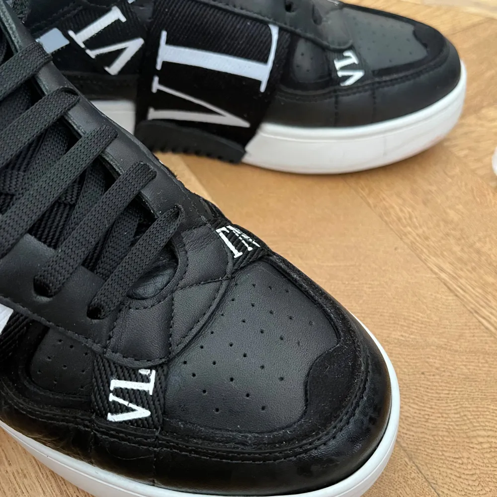 Säljer ett par snygga svarta sneakers från Valentino Garavani. Skorna har en cool design med vita detaljer och texten 'VLTN' på sidan. De är gjorda i skinn och har en bekväm passform med snörning. Perfekta för både vardag och fest!. Skor.