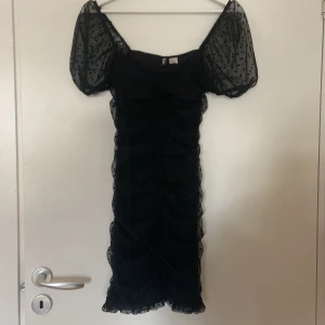 Svart klänning från H&M - Säljer en superfin svart klänning från H&M i storlek XS. Den har puffiga kortärmar med ett prickigt mönster och en tight passform som ger en snygg siluett. Perfekt för festliga tillfällen! 💃