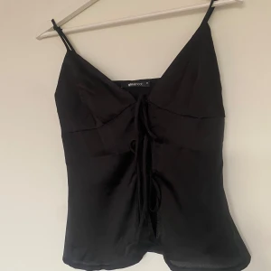 Svart satinlinne  - Snygg svart satinlinne från Ginatricot med smala axelband och knytning framtill. Perfekt för en stilren look. Passar bra till både jeans och kjol.