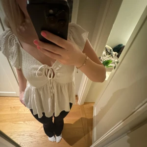 Vit blus med knytning - Charmig vit blus med knytning framtill och volangdetaljer. Den har korta ärmar och en luftig passform, perfekt för en avslappnad stil. Materialet är lätt och bekvämt.🩷