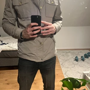 Beige jacka från J.Lindeberg - Snygg beige jacka från J.Lindeberg med dragkedja och knappar. Jackan har flera praktiska fickor och en stilren design. Perfekt för en casual look. Hör av er ifall ni undrar något! Ps! Jag har M och använder jackan