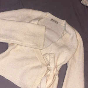 Vit omlottkofta från Gina tricot  - Säljer en mysig vit omlottkofta med knytband i midjan. Koftan är stickad och har långa ärmar. Använd en gång! Koftan är slutsåld på ginas hemsida❣️skulle säga att färgen är gräddvit. ( färgen på koftan skiljer sig på bilderna pga gult ljus i mitt rum)